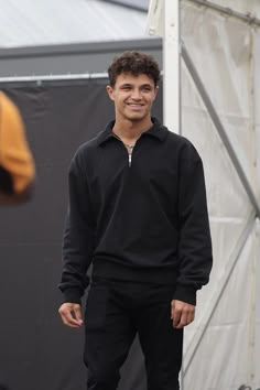 a young man standing in front of a white tent wearing black sweatpants and smiling