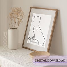 a white vase sitting on top of a table next to a wooden framed map with the state of california