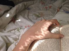 a person laying in bed reading a book with their hand on top of the book