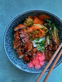 a bowl filled with meat, vegetables and chopsticks on top of a blue table