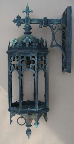 an ornate blue metal wall light hanging from the side of a white wall with crosses on it