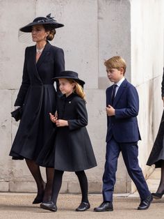 two children and an older woman are walking down the street with their mother, who is wearing a black hat