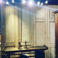 an old desk and chair in front of wooden cupboards with lights on the wall