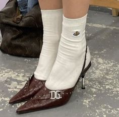 a woman's legs wearing white socks and brown shoes, with her purse in the background