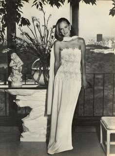 a woman standing in front of a window wearing a white dress and posing for the camera