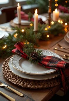 a christmas table setting with candles and plaid napkins on the placemat, pine cone centerpiece