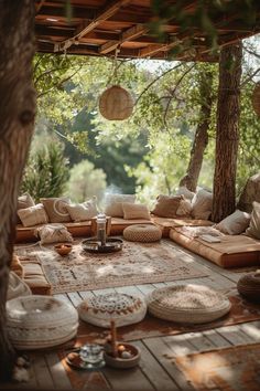 an outdoor area with lots of pillows and rugs on the ground, surrounded by trees