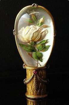 a white rose in a glass dome with gold trim on a black surface, surrounded by green leaves