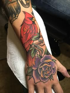 a person's hand with a red bird and flowers tattoo on the left arm