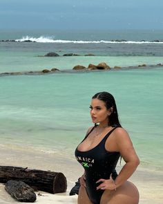 a beautiful woman in a black bathing suit standing on the beach next to a log