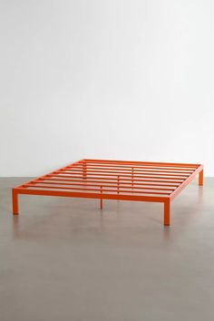 an orange bed frame sitting on top of a cement floor next to a white wall