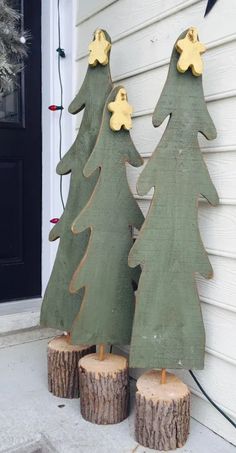 three wooden christmas trees sitting next to each other on top of a tree stump in front of a house