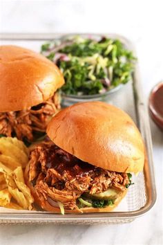 two pulled pork sandwiches with lettuce, pickles and chips on a tray