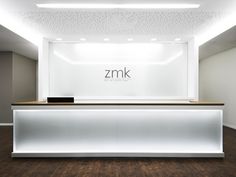 an empty white reception area with wooden flooring and lights on the ceiling, along with a sign that reads zmk