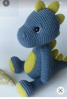 a crocheted blue and yellow dragon stuffed animal sitting next to a birthday cake