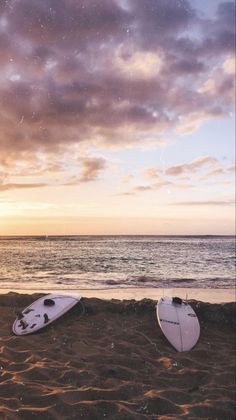 two surfboards sitting on top of a sandy beach next to the ocean under a cloudy sky