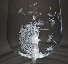 a wine glass with white dandelions etched on the bottom and inside, sitting on a table