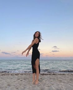 a woman standing on top of a sandy beach next to the ocean with her arms in the air