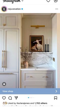 a white kitchen with marble counter tops and cabinets in the middle, along with a painting on the wall