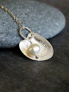 a silver necklace with a pearl in the center on a stone surface next to a rock