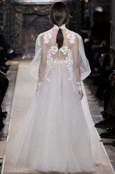 a model walks down the runway in a white dress with sheer sleeves and flowers on it