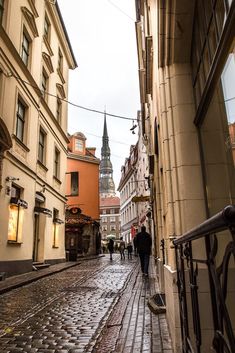 people are walking down an alleyway between two buildings with steeples in the background