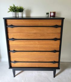 a wooden dresser with black metal handles and two potted plants on top of it