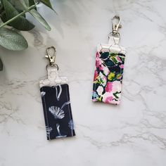 two keychains with flowers on them sitting next to a plant