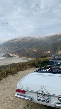 an old white car parked on the side of a dirt road next to the ocean