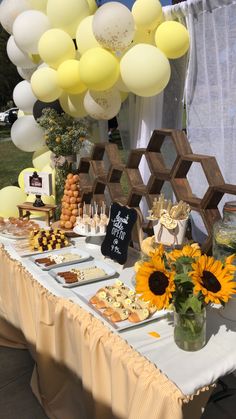 a table with sunflowers, cake and balloons in the shape of honeycombs