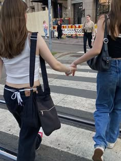 two girls walking down the street holding hands with each other and carrying bags on their backs