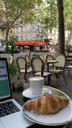 an open laptop computer sitting on top of a table next to a croissant