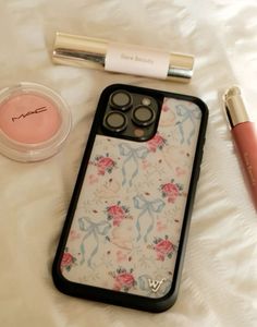 an iphone case sitting on top of a white bed next to lipstick and makeup brush