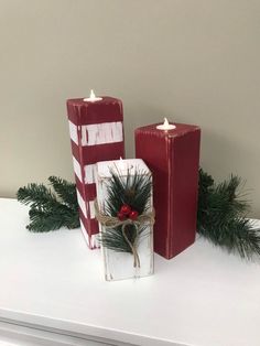 two red and white candles sitting on top of a table next to each other with pine branches