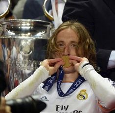 a man holding a gold medal in front of his face while sitting next to a trophy