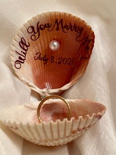 two seashells with wedding rings in them on a white table cloth, the shell has writing on it