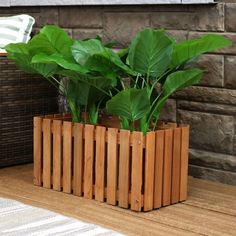 a wooden planter filled with green plants on top of a hard wood floor next to a brick wall