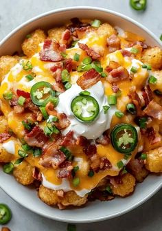 a white bowl filled with tater tots covered in cheese and green pepper slices