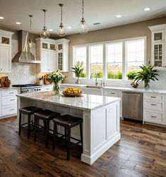 a large kitchen with white cabinets and wooden flooring, along with two stools at the center island