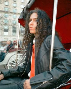 a woman with long curly hair sitting under an umbrella