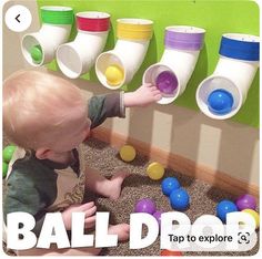 a toddler playing with balls on the floor in front of a wall filled with cups