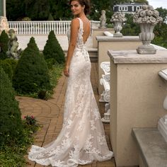 a woman in a white wedding dress standing on a brick walkway next to some bushes