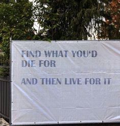 a large white sign with words on it in front of a fence and some trees