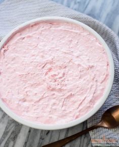 a white bowl filled with pink cream next to two spoons