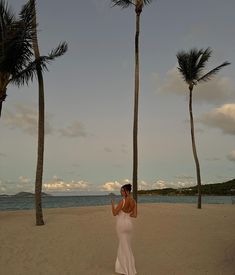 a woman standing on top of a sandy beach next to palm trees and the ocean