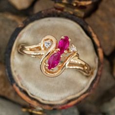 a gold ring with two diamonds and a pink stone in the middle, sitting on top of a rock