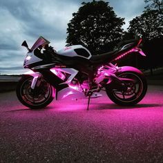 a motorcycle that is sitting in the street with pink lights on it's side