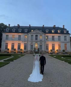 a bride and groom walking in front of a large mansion at night with lights on