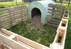 a dog house made out of wooden pallets in the grass next to a fence