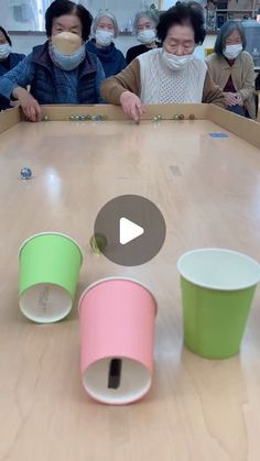 people wearing face masks sitting around a table with cups on it and one person in the middle